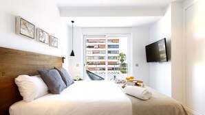 Een moderne hotelkamer met een groot bed, een flatscreen-tv aan de muur en een balkon met uitzicht over de stad.