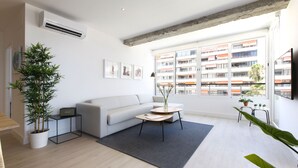Een moderne woonkamer met een witte bank, een salontafel en een groot raam met uitzicht op een gebouw.