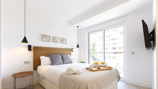 Een moderne slaapkamer met een houten hoofdbord, een nachtkastje, een bed met een beige sprei, en een dienblad met glazen en een boek.