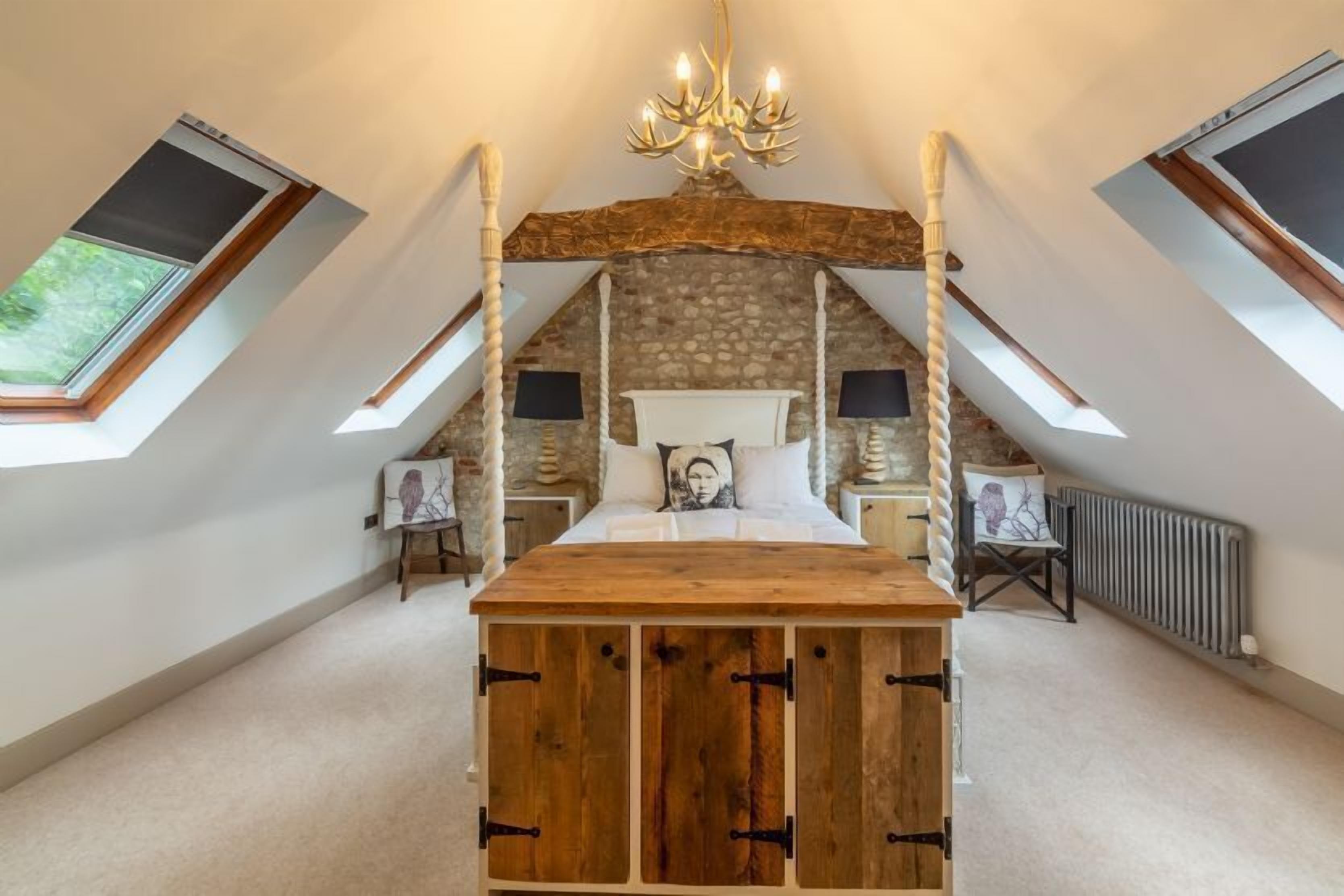 A bedroom with a sloped ceiling, a wooden bed frame, a stone wall, and a skylight.