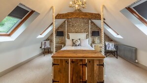 A bedroom with a sloped ceiling, a wooden bed frame, a stone wall, and a skylight. - Hideaway Barn (4), Thornham, Norfolk (Thornham)