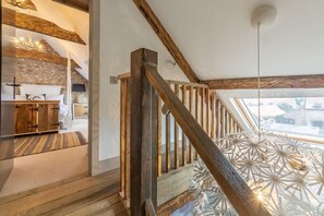 Una escala de fusta amb vista a una habitació que destaca per una paret de pedra i un llit.