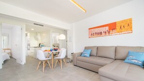 Ett modernt vardagsrum med en beige soffa, ett matbord med stolar och ett kök i bakgrunden.