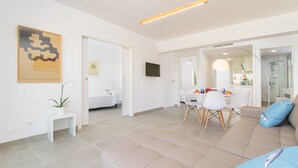 Ett modernt vardagsrum med en beige soffa, en matplats med vita stolar och ett litet vitt bord.
