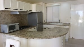 Eine moderne Küche mit weißen Schränken, einem Edelstahl-Kühlschrank, einer Mikrowelle und einer Arbeitsplatte aus Granit.