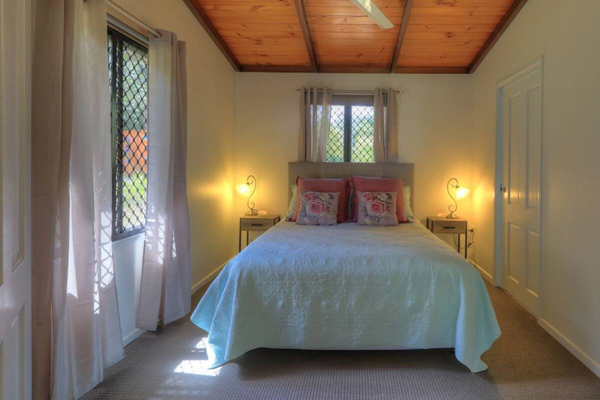 A bedroom with a bed, two bedside tables, a window with curtains, and a door.