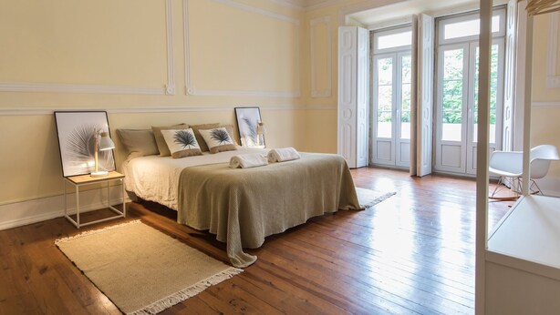 Ein geräumiges Schlafzimmer mit einem großen Bett, einem Nachttisch, einem Sessel und Blick ins Freie durch eine Glastür.