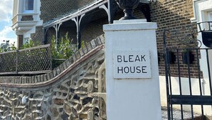 Un bâtiment historique à la façade en pierre, doté d’une tourelle et d’une enseigne portant l’inscription « BLEAK HOUSE ».