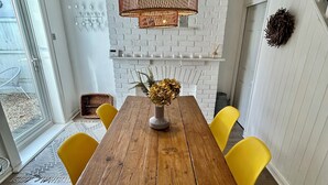 Un espace repas avec une table en bois, des chaises jaunes, un luminaire suspendu et un mur en briques blanches.