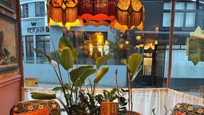 Un coin salon accueillant avec des fauteuils et des poufs aux motifs variés, une petite table avec une boisson et un luminaire décoratif suspendu.