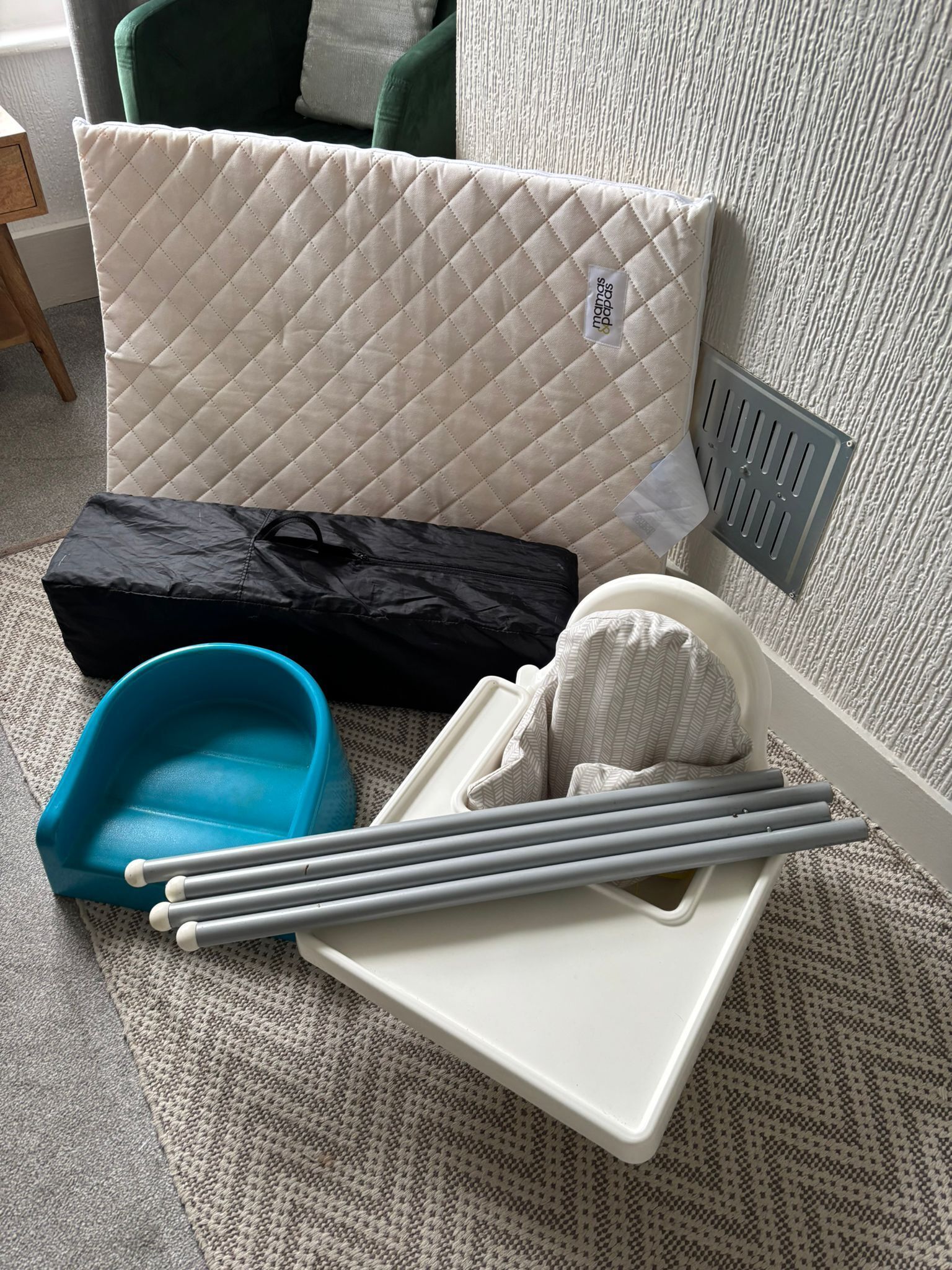 Un lit avec une tête de lit matelassée, un sac noir, un récipient bleu et un plateau avec un tissu blanc et des bâtonnets gris.
