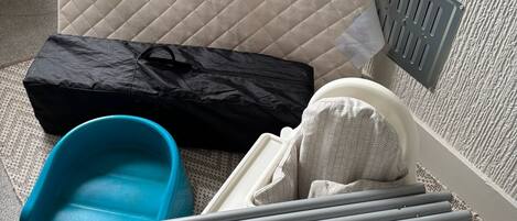 Un lit avec une tête de lit matelassée, un sac noir, un récipient bleu et un plateau avec un tissu blanc et des bâtonnets gris.