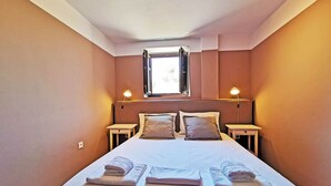 Une chambre à coucher comprenant un lit, deux tables de chevet, une fenêtre et deux lampes fixées au mur.