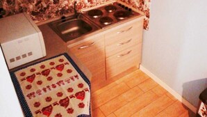 A compact kitchen with wooden cabinets, a stove, and a tiled backsplash. - My House of Milan 19 (Milano)