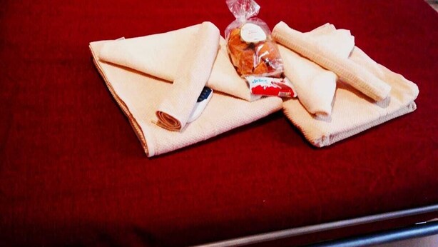 A neatly made bed with a red blanket, pillows, and folded towels. - My House of Milan 19 (Milano)