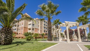 A hotel courtyard with palm trees, a brick pathway, and a white pergola structure. - Las Arenas - Haraganes Beach HLHA215P214 (Isla Canela)