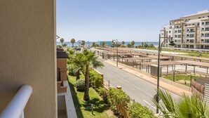 A view from a balcony overlooking a road with a pedestrian bridge, palm trees, and a building with multiple floors. - Las Arenas - Haraganes Beach HLHA215P214 (Isla Canela)