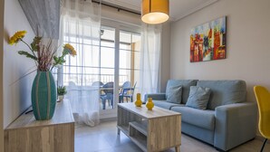 A living room with a sofa, a coffee table, a vase with flowers, and a painting on the wall. - Las Arenas - Haraganes Beach HLHA215P214 (Isla Canela)