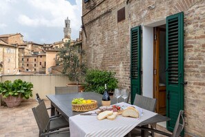A table set outdoors with a bottle, glasses, bread, and a fruit basket. - HOUSE WOW panoramic terrace *.* (Siena)