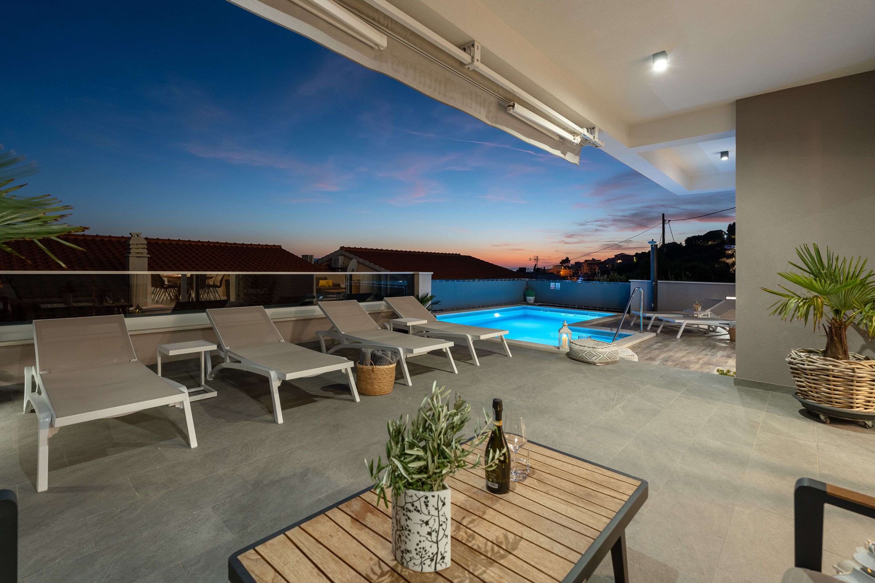 A rooftop terrace with lounge chairs, a pool, and a table with a bottle and glass.
