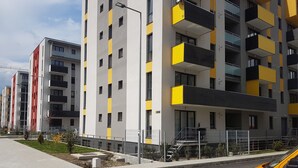 Ein modernes Mehrfamilienhaus mit Balkonen, einem gepflasterten Bürgersteig und einem gelben Auto im Vordergrund.