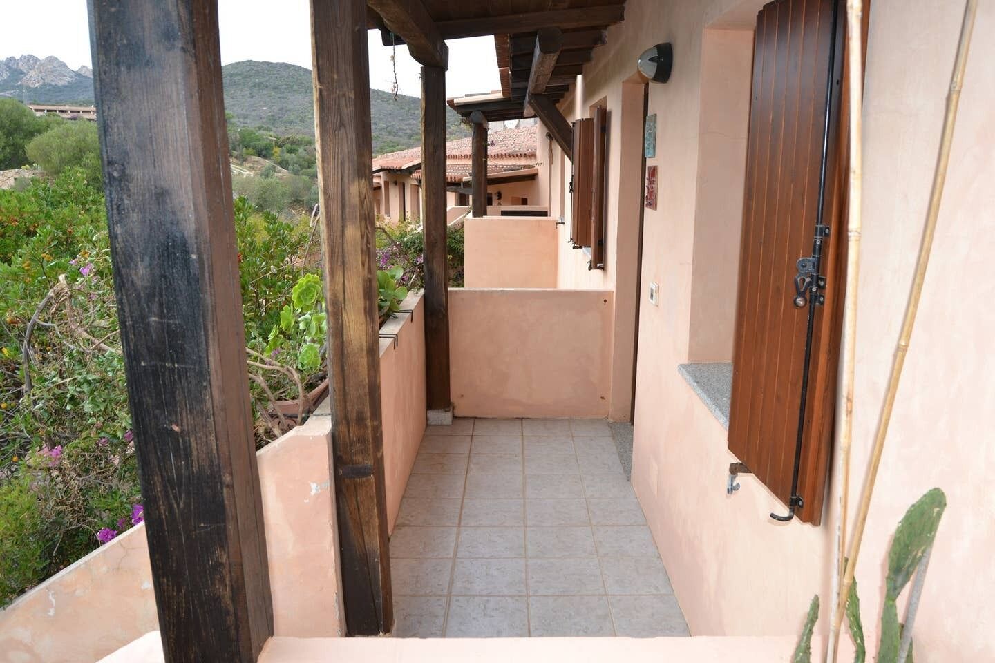 Un pasillo estrecho con pilares de madera, paredes color beige y suelo de baldosas que conduce a una puerta.