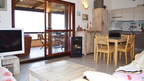 Un salon comprenant un téléviseur, une cheminée, un coin repas avec des chaises et une cuisine équipée de placards.
