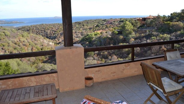 Une terrasse offrant une vue sur un paysage côtier, avec des collines et une étendue d’eau.