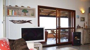 Un salon comprenant un téléviseur, un canapé, une table basse en bois et une porte-fenêtre coulissante donnant sur une terrasse extérieure.