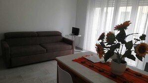 Een woonkamer met een bank, een eettafel met een vaas zonnebloemen en een tv op een dressoir.