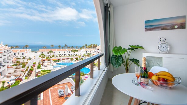 Ein Balkon mit Blick auf ein Resort, ein Tisch mit Champagnerflasche, einem Glas und einer Obstschale.