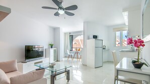 Ein modernes Wohnzimmer mit einem Glastisch, einer Couch, einem Flachbildfernseher und einem Deckenventilator.
