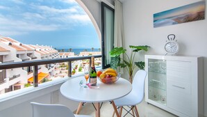 Ein Balkon mit Tisch, Stühlen, einer Champagnerflasche, einer Obstschale und einer Uhr auf einem Schrank.