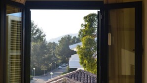 Blick durch ein Fenster auf eine Straße, Bäume und ein Gebäude mit Ziegeldach.