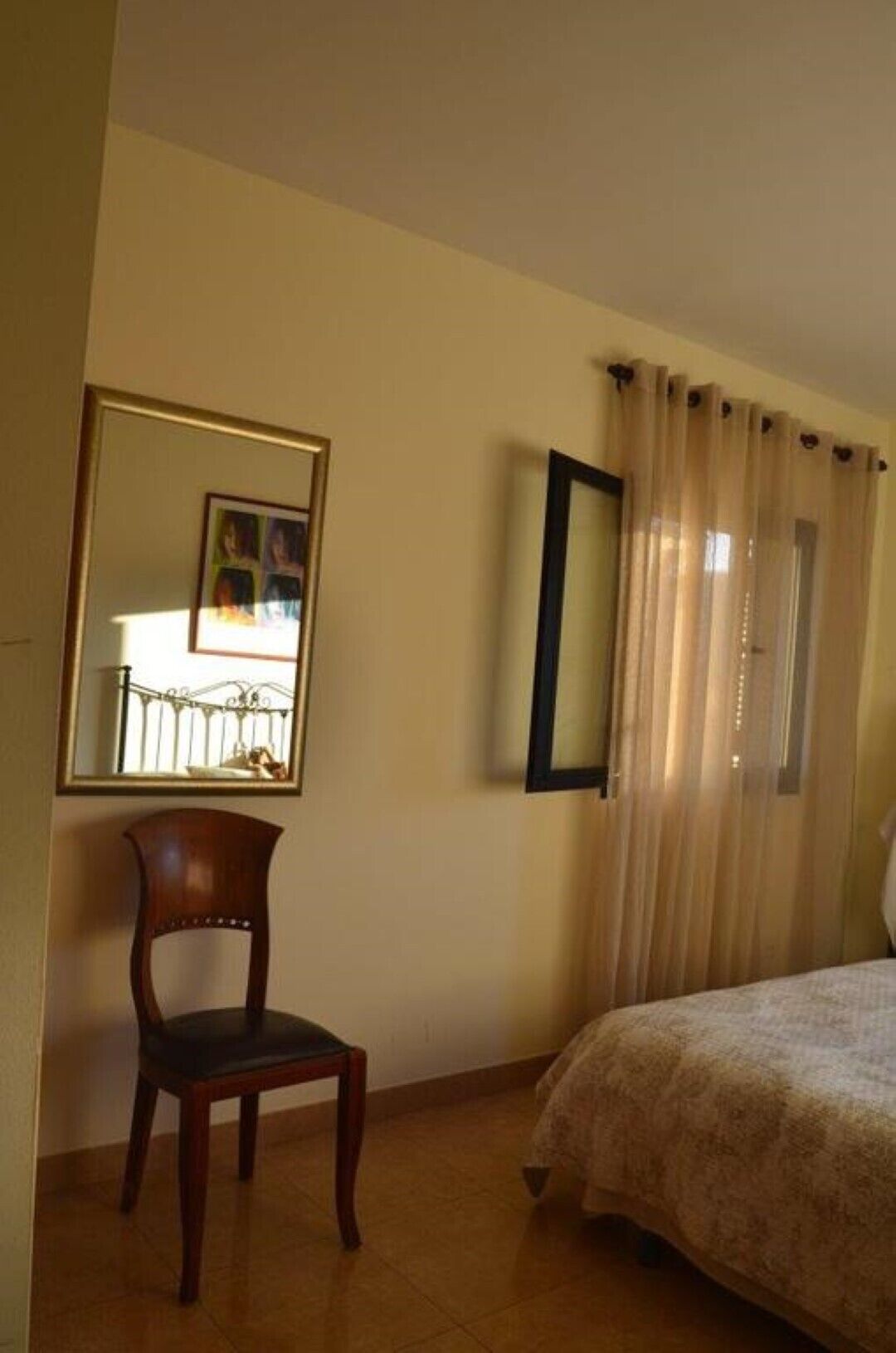 A bedroom with a bed, a chair, a mirror, and curtains.