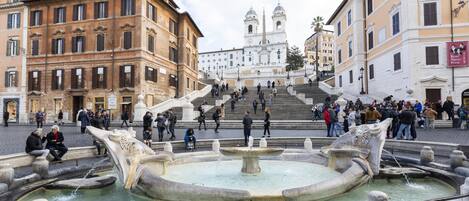 A public square with a fountain, steps leading to a church, and surrounding historic buildings.