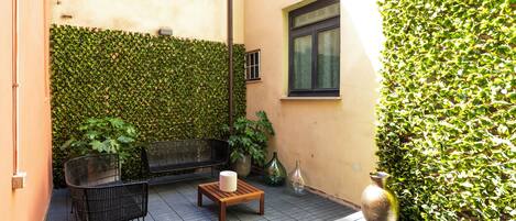 A small patio with a wooden table, two chairs, and a potted plant.
