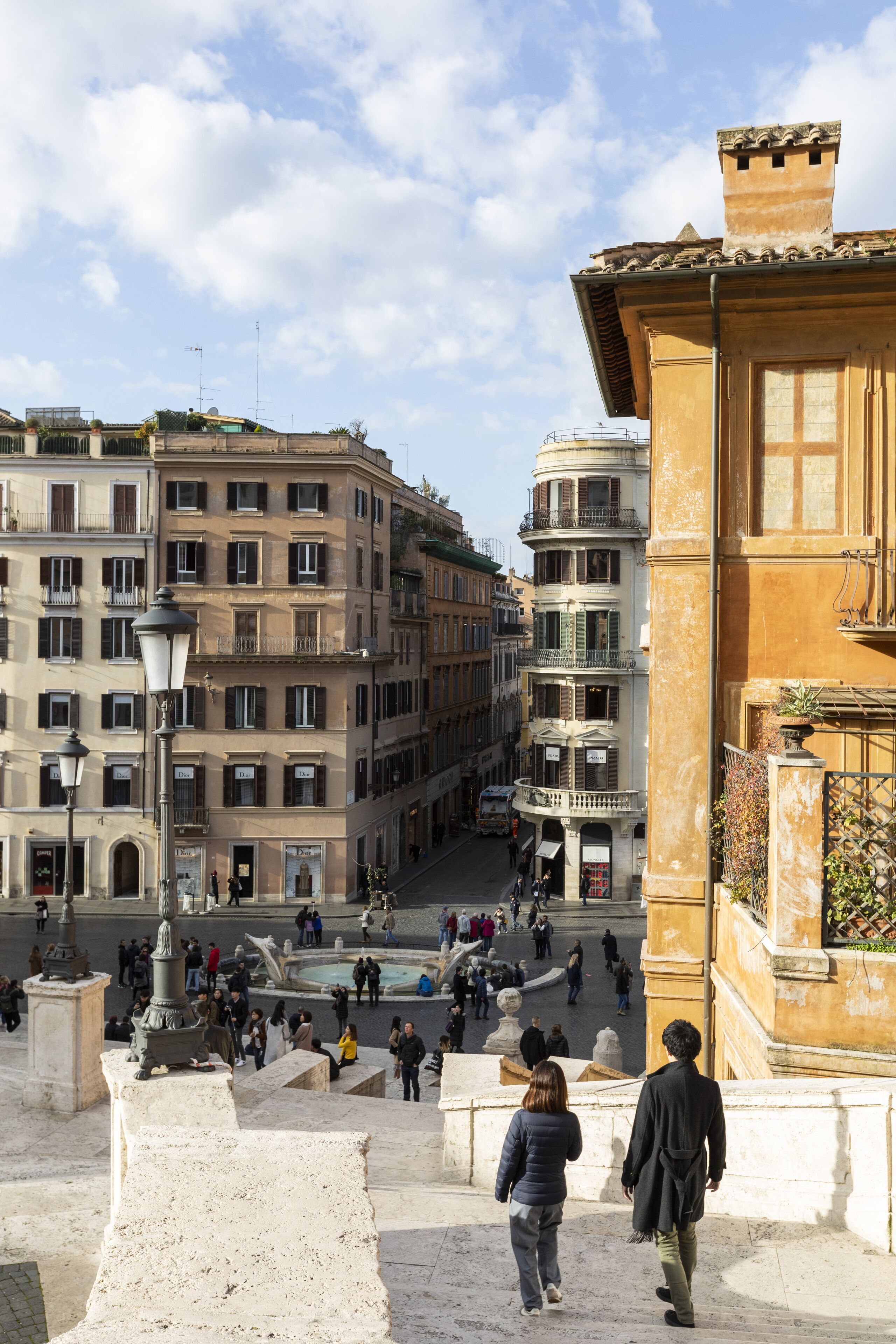 A historic building with classical architecture, a public square with people, and a fountain.