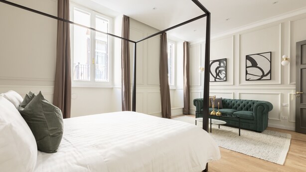 Ein Schlafzimmer mit einem Himmelbett, einem grünen Sofa und Kunstwerken an den Wänden.