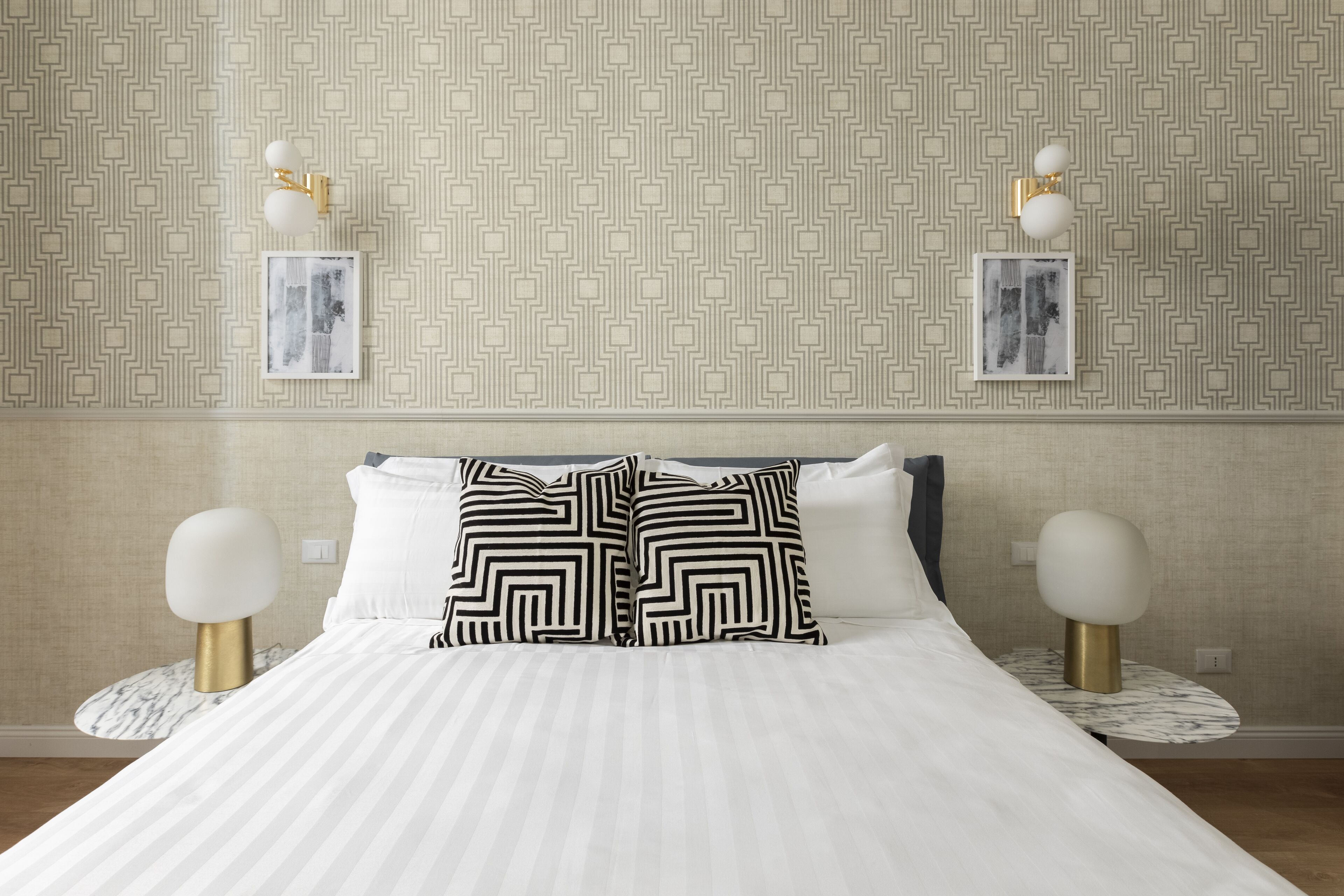 Cama bem arrumada com roupa de cama listrada, duas almofadas com padrão preto e branco e um abajur dourado e branco.