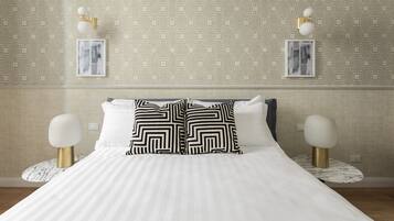 Cama bem arrumada com roupa de cama listrada, duas almofadas com padrão preto e branco e um abajur dourado e branco.