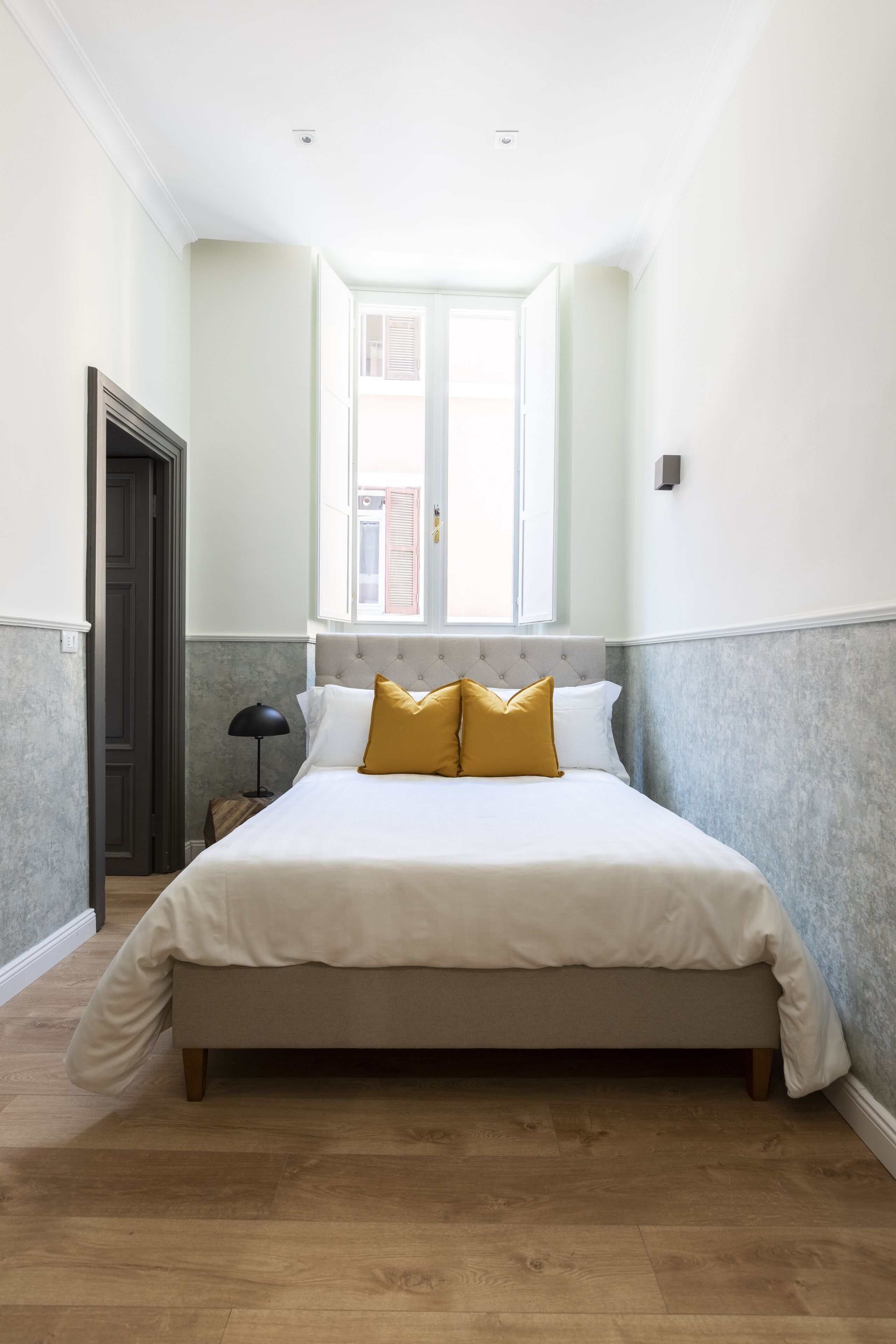 A neatly arranged bedroom with a large bed, a window, and a nightstand.