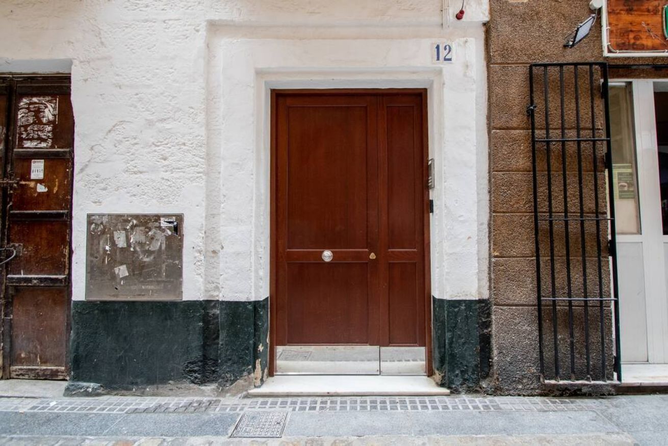 A building with a brown door, white and green painted walls, and a black metal gate.