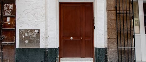 A building with a brown door, white and green painted walls, and a black metal gate.