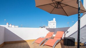 Una terrazza sul tetto con due poltrone arancioni, un ampio ombrellone beige e un edificio bianco sullo sfondo.