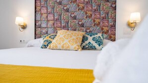 Una camera d'albergo con un letto, cuscini decorativi, una coperta gialla e una parete a motivi floreali.