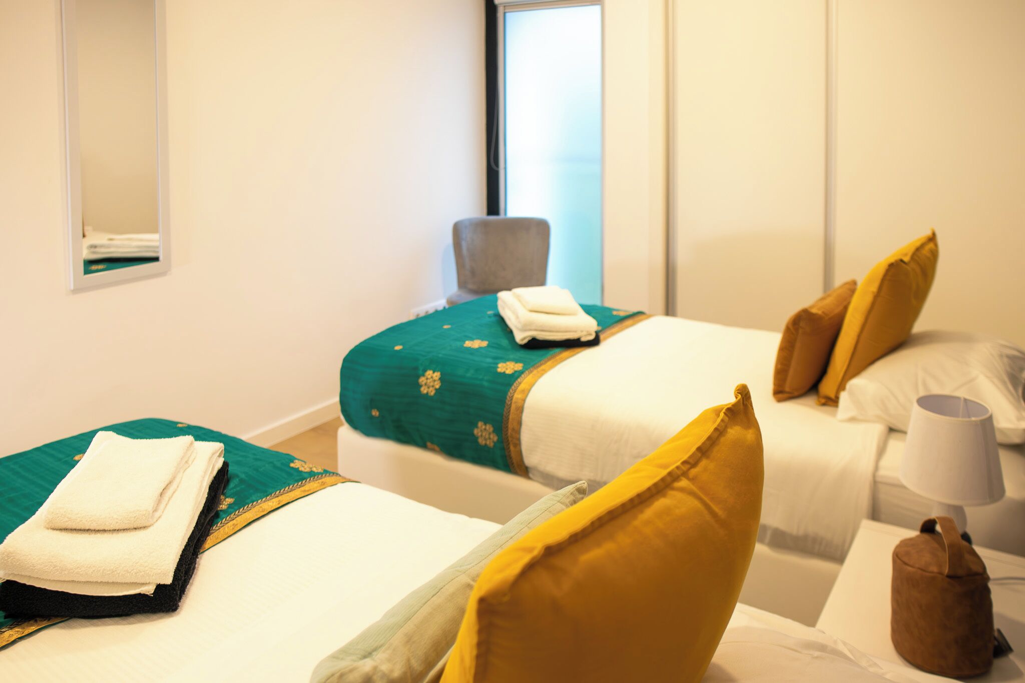 A hotel room with two beds, a chair, a lamp, and a window.