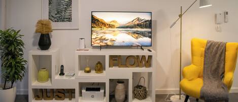 A modern living room with a flat-screen TV, a yellow armchair, and a white shelving unit with decorative items.
