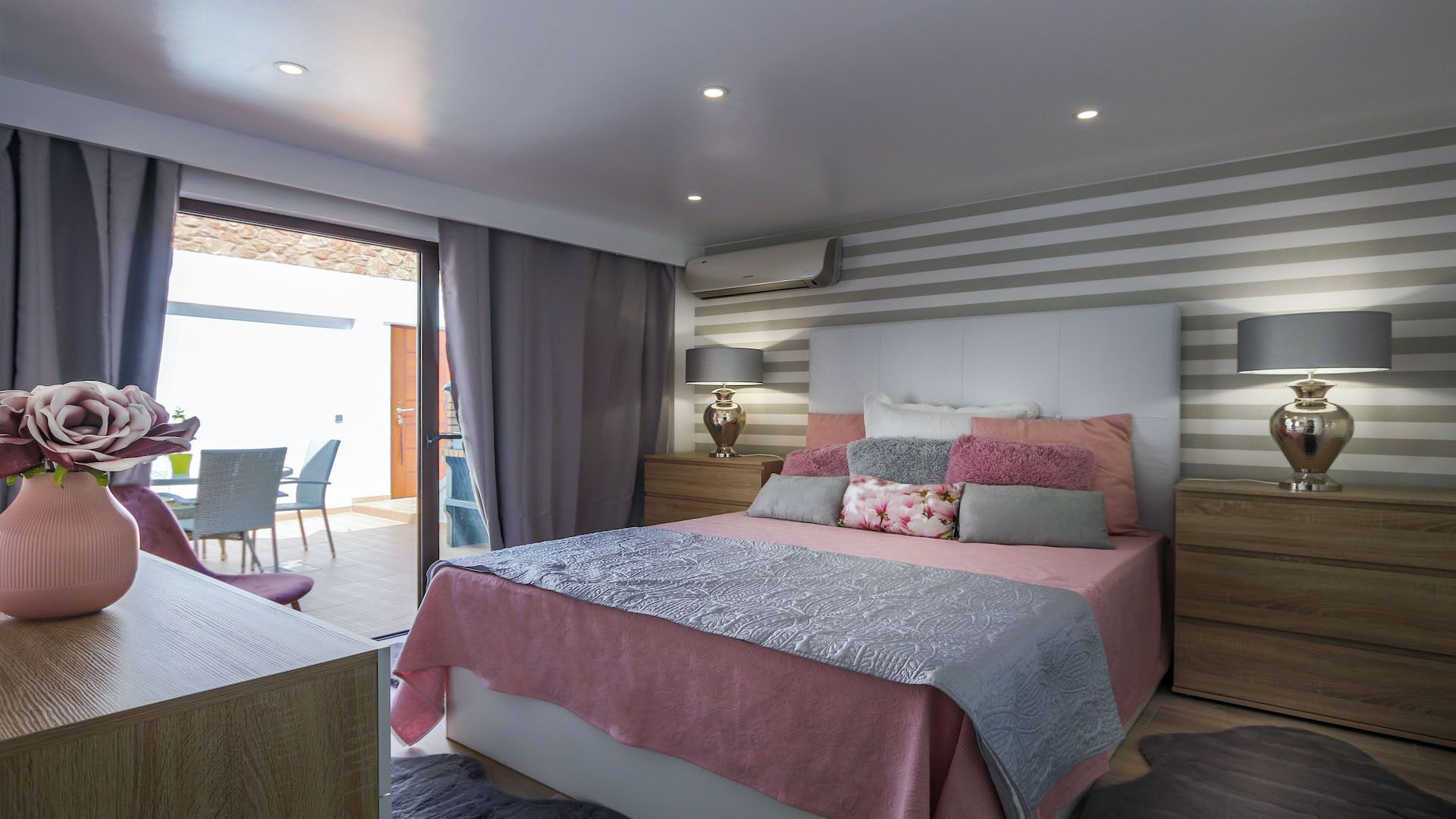 Un dormitorio moderno con cama, lámparas de noche, cómoda y vista al exterior.