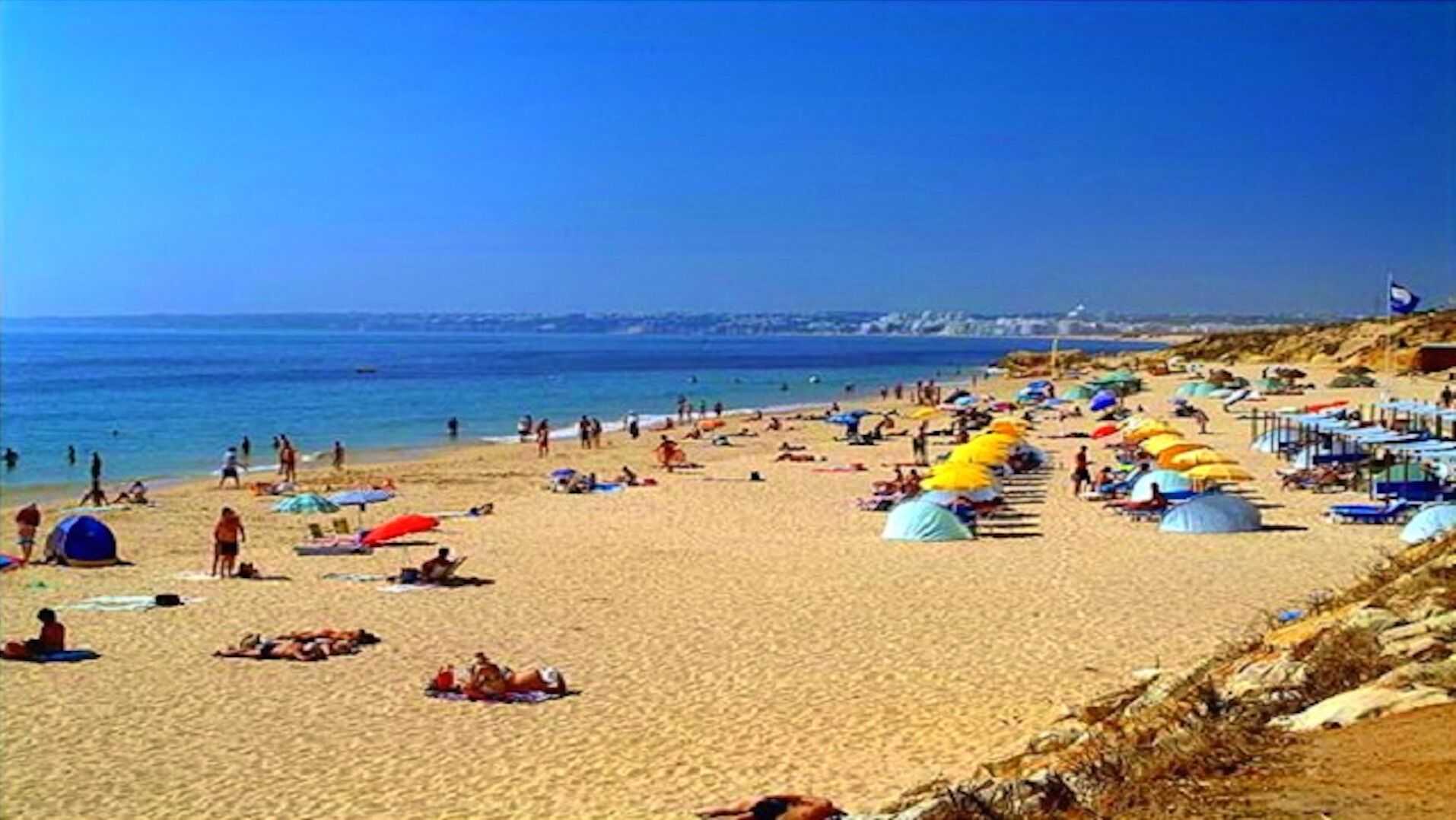 Una playa con tiendas de campaña y sombrillas, gente tomando el sol y nadando.